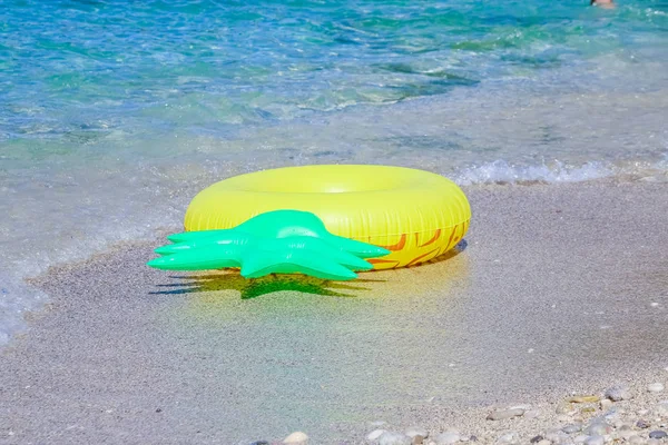Yellow inflatable paddling circle in shape of pineapple in the sand near the sea.ring floating near the beach,Colorful inflatable ring for swimming.Copy space — стоковое фото